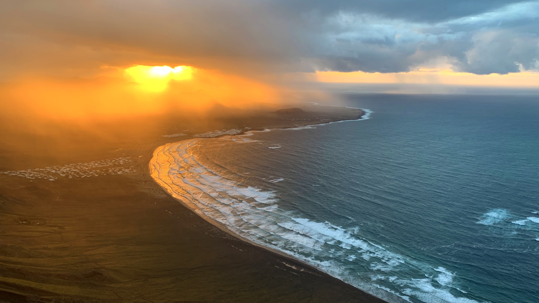 Storm light over Famara beach, Lanzarote — golden sun breaking over the Atlantic surf
