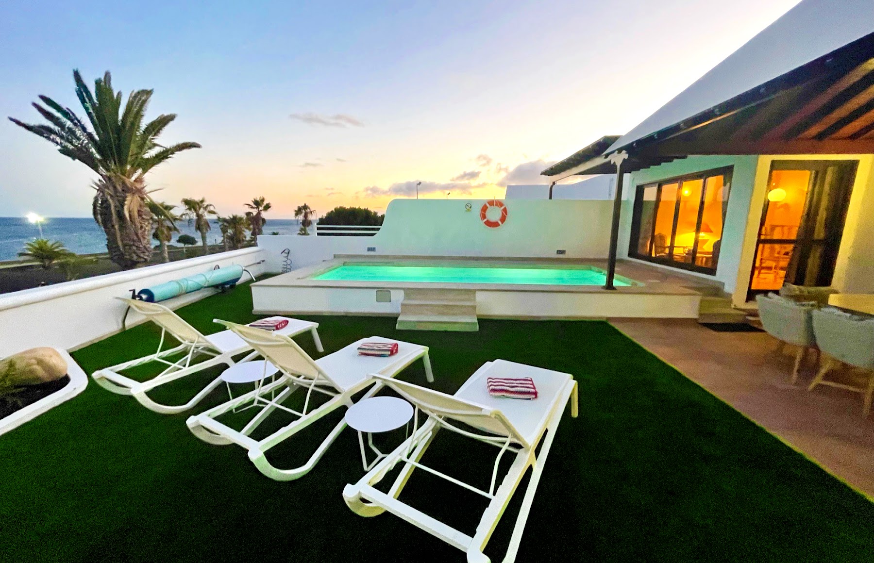 Loungers on the villa's lawn beside the pool, ocean sunset beyond