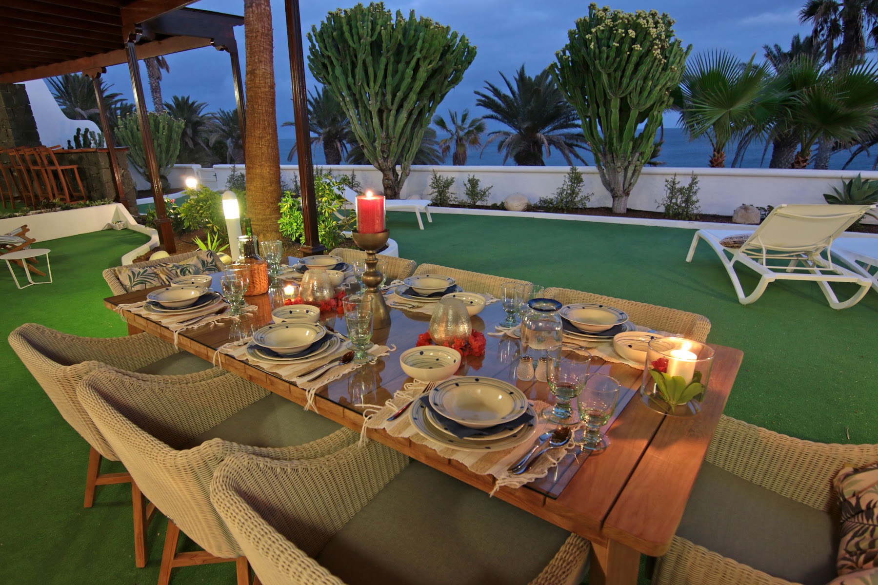 Candle-lit dinner table on the villa's lawn, cacti and ocean beyond