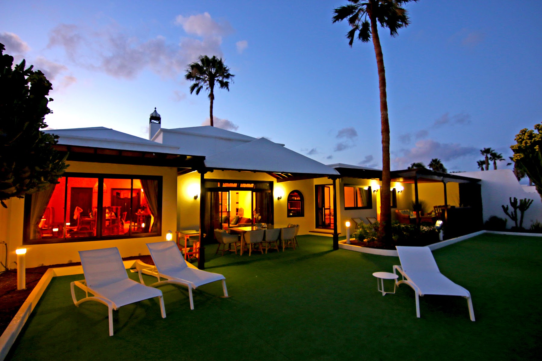 Villa Vista del Mar glowing at dusk — lawn, loungers and palm trees
